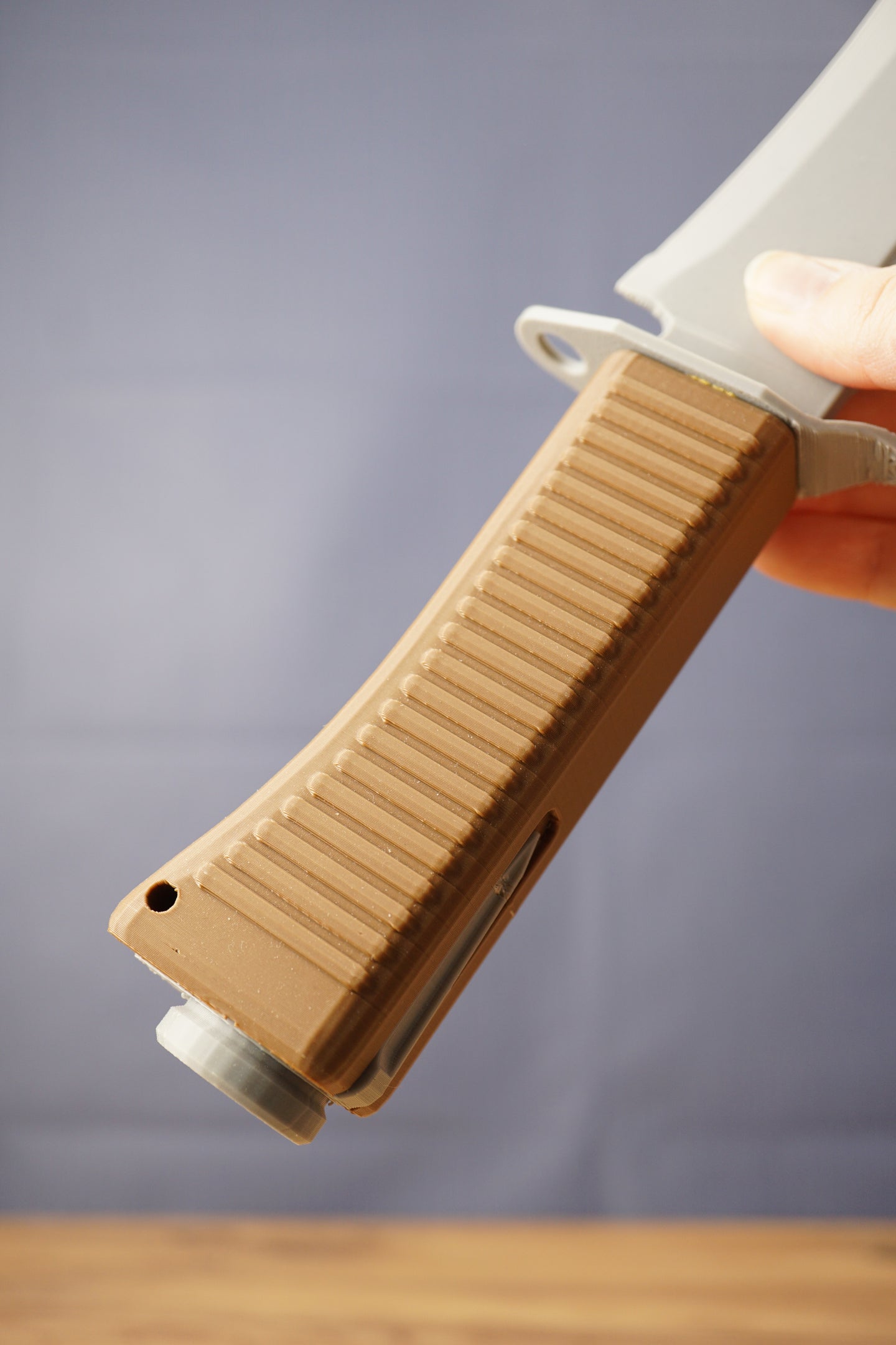 Close-up of the brown ribbed handle on a 3D-printed survival machete replica, held against a gray background.