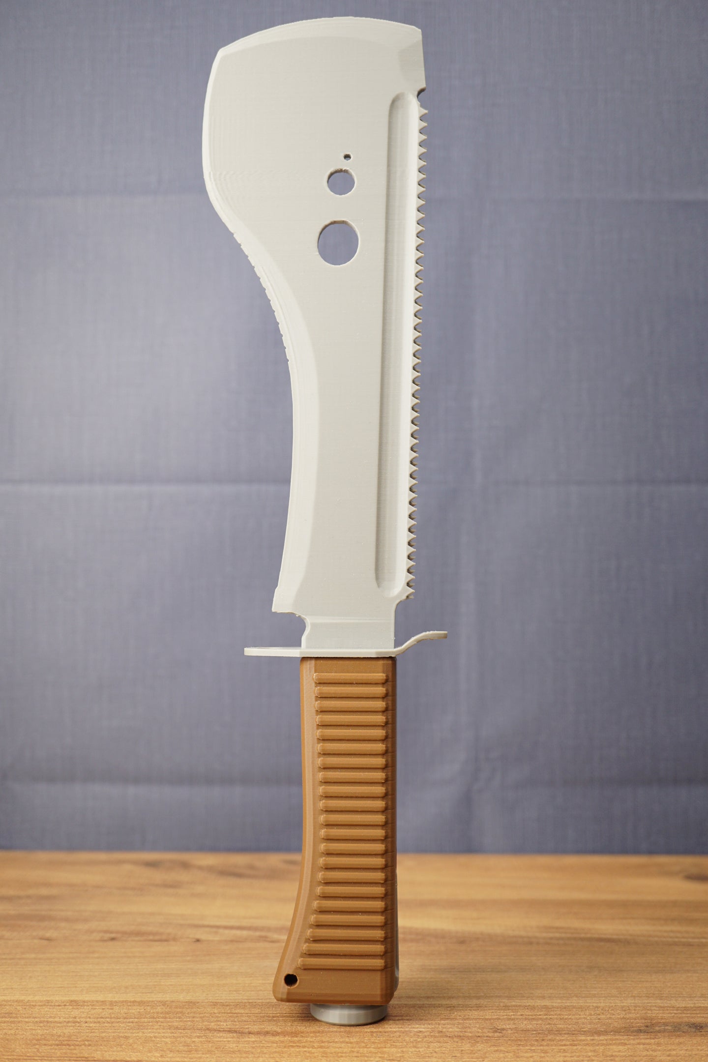 Full upright view of a 3D-printed UVSR Taiga-1 survival machete replica standing on a wooden table, featuring a gray blade and brown ribbed handle.