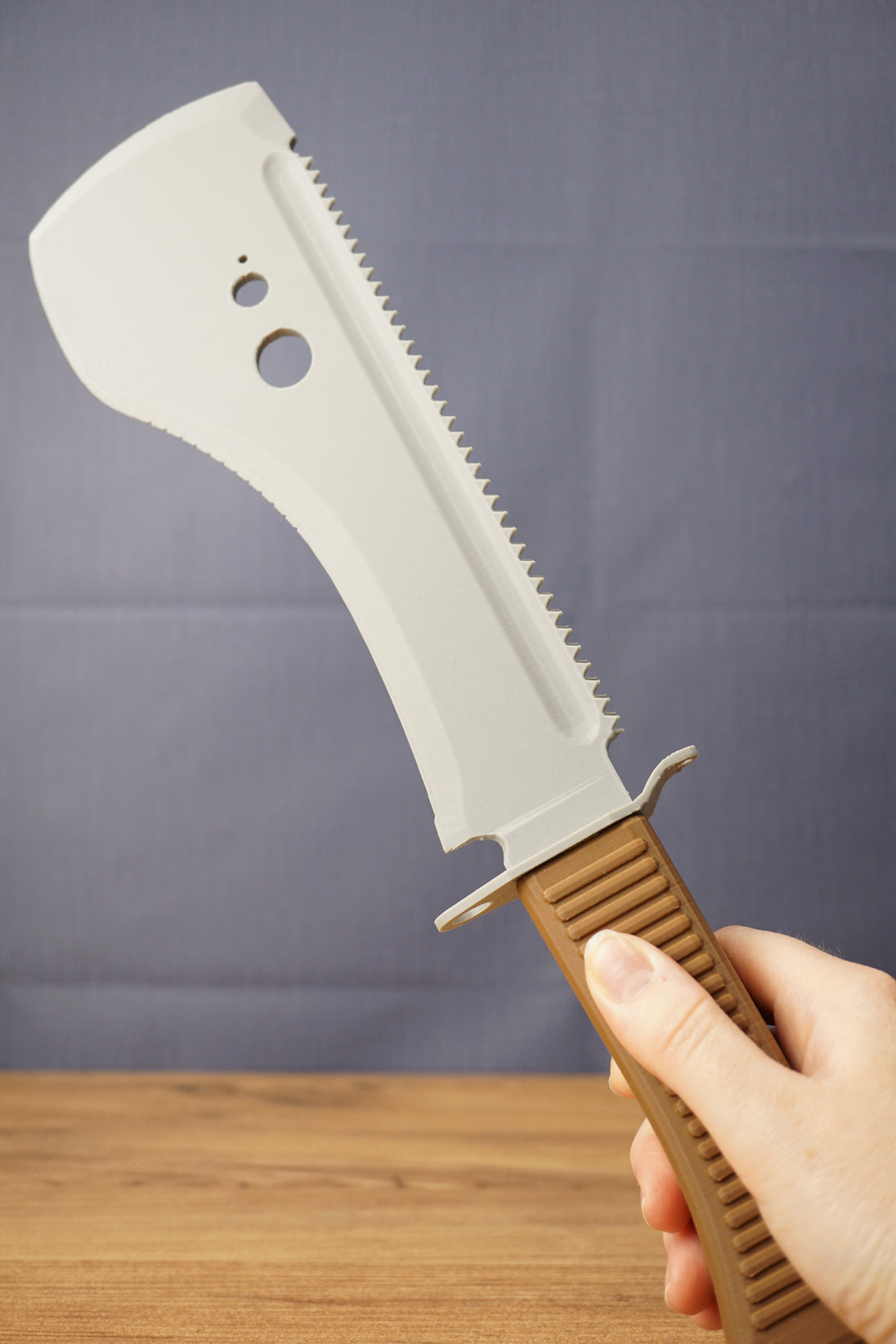 Hand holding a 3D-printed UVSR Taiga-1 survival machete replica with a gray blade and brown textured handle.