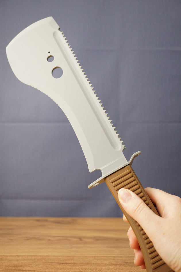 Hand holding a 3D-printed UVSR Taiga-1 survival machete replica with a gray blade and brown textured handle.