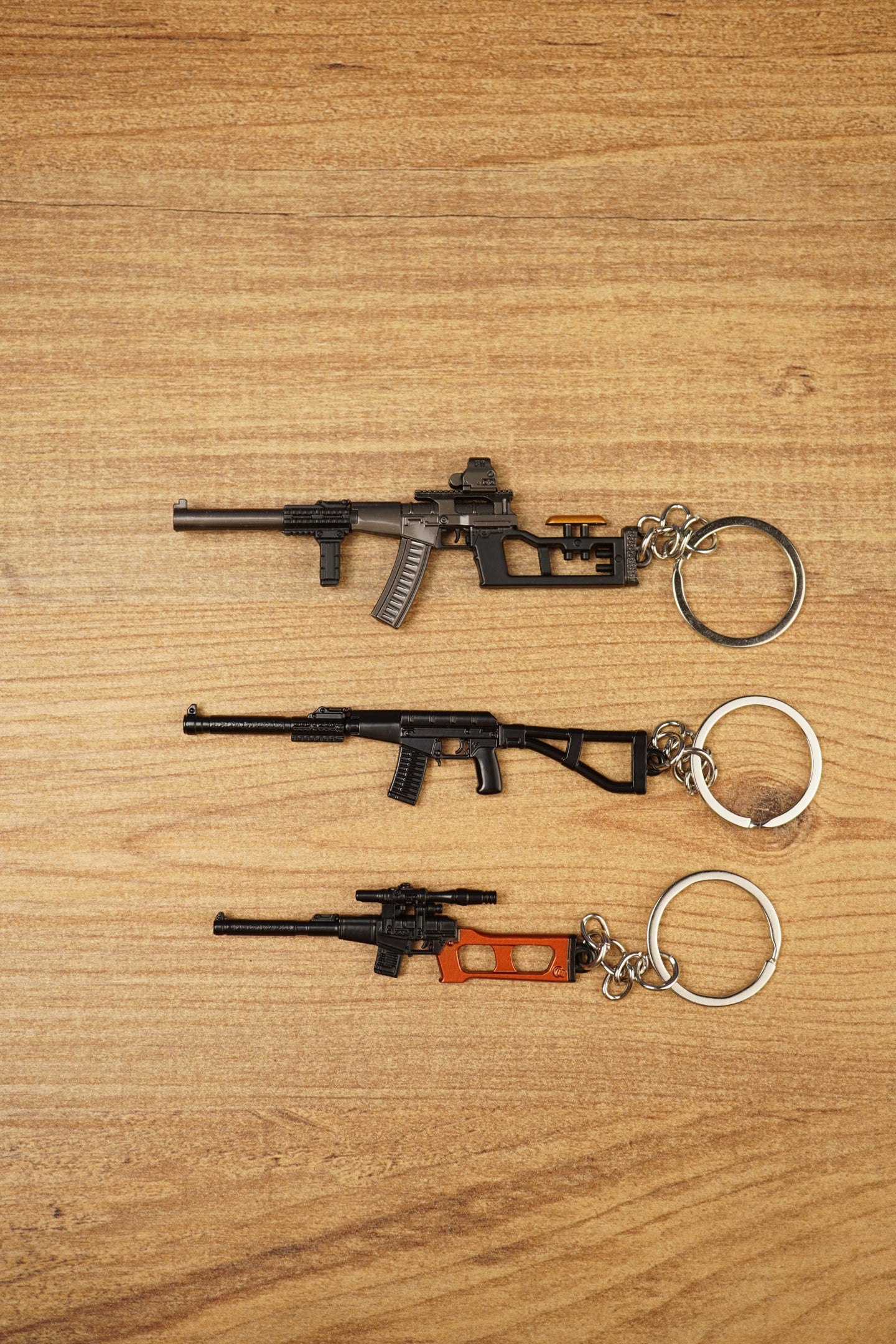Three VSS Vintorez and AS Val style rifle keychains displayed on a wooden surface, showing base, modded and scoped tactical variants