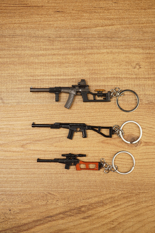 Three VSS Vintorez and AS Val style rifle keychains displayed on a wooden surface, showing base, modded and scoped tactical variants