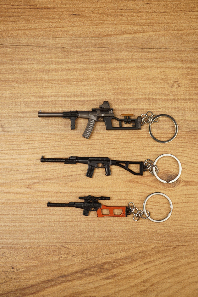 Three VSS Vintorez and AS Val style rifle keychains displayed on a wooden surface, showing base, modded and scoped tactical variants