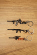 Three VSS Vintorez and AS Val style rifle keychains displayed on a wooden surface, showing base, modded and scoped tactical variants