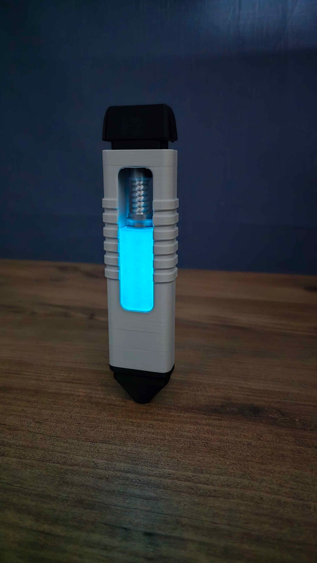 WARDOGS Adrenaline Pen replica standing upright on a wooden table in low light, showing the glowing blue panel, white grip and visible silver mechanism.