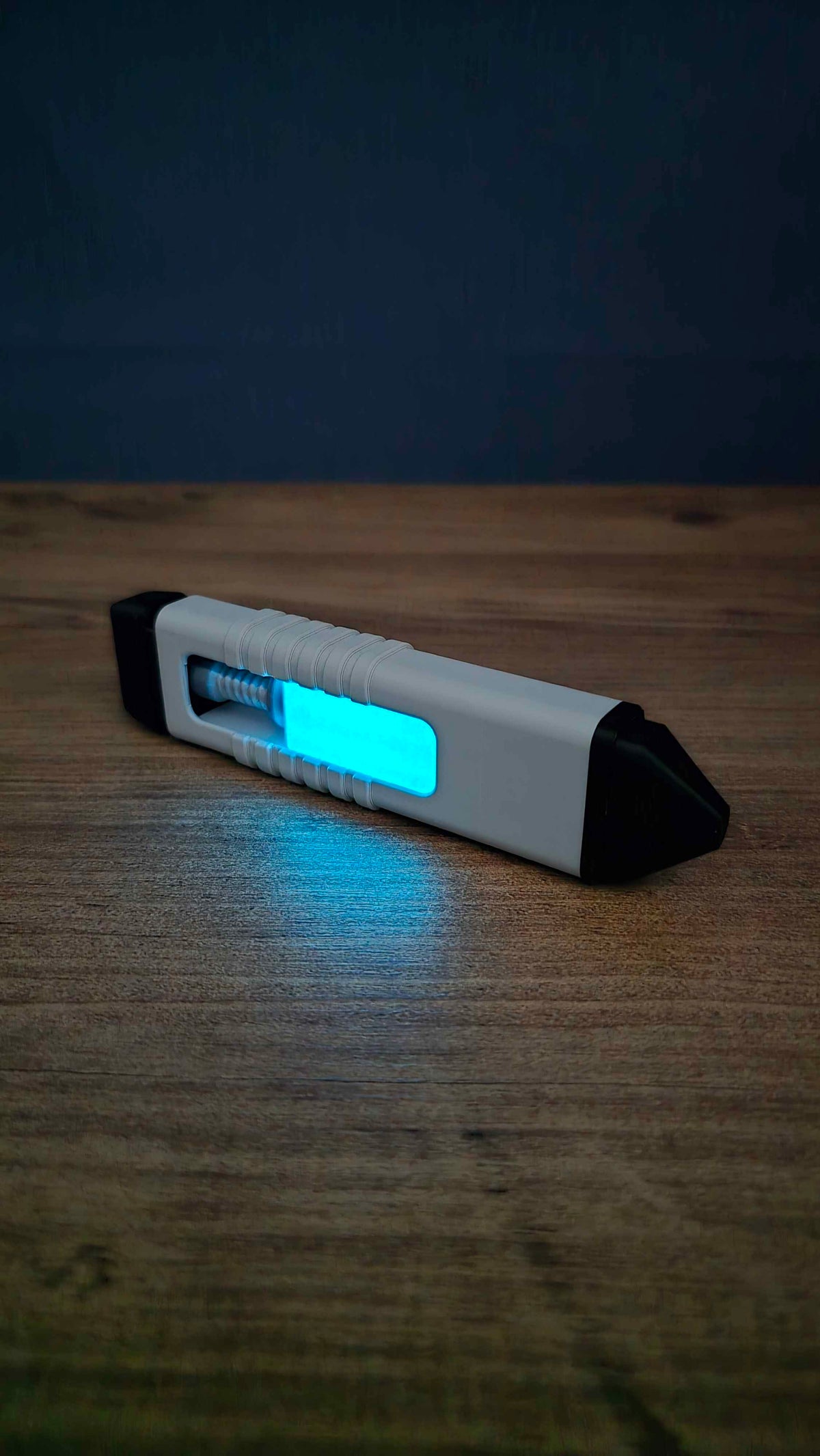WARDOGS Adrenaline Pen fidget clicker with bright blue glow in the dark centre, casting a cyan reflection onto the wooden tabletop beside it.