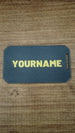 Reverse side of a personalised WARDOGS Alpha Card 1 gaming keycard with a custom name in bold yellow lettering on a textured dark grey surface.
