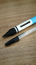 WARDOGS Adrenaline Stim Pen replica with fitted ballpoint writing tip exposed, positioned beside a transparent BIC-style pen for comparison.