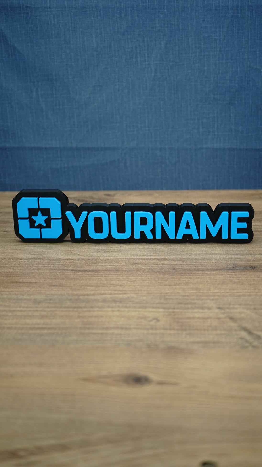 Lonestar Blue faction gaming nameplate with raised blue YOURNAME lettering, a star emblem and black backing, photographed standing on a wooden desk.