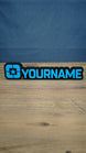 Lonestar Blue faction gaming nameplate with raised blue YOURNAME lettering, a star emblem and black backing, photographed standing on a wooden desk.