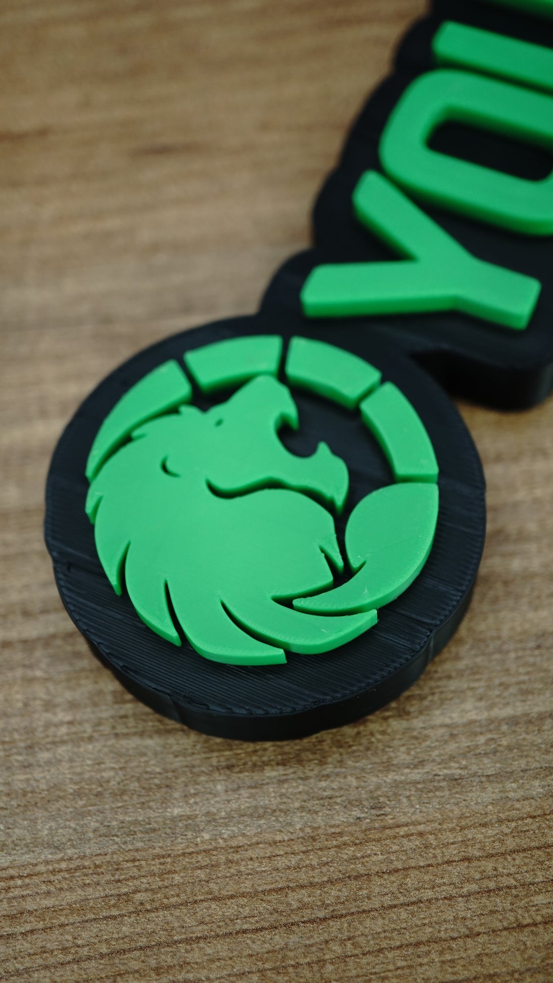 Close-up of the Manticore Green lion faction emblem with bright green raised detailing, a circular design and contrasting black nameplate backing.