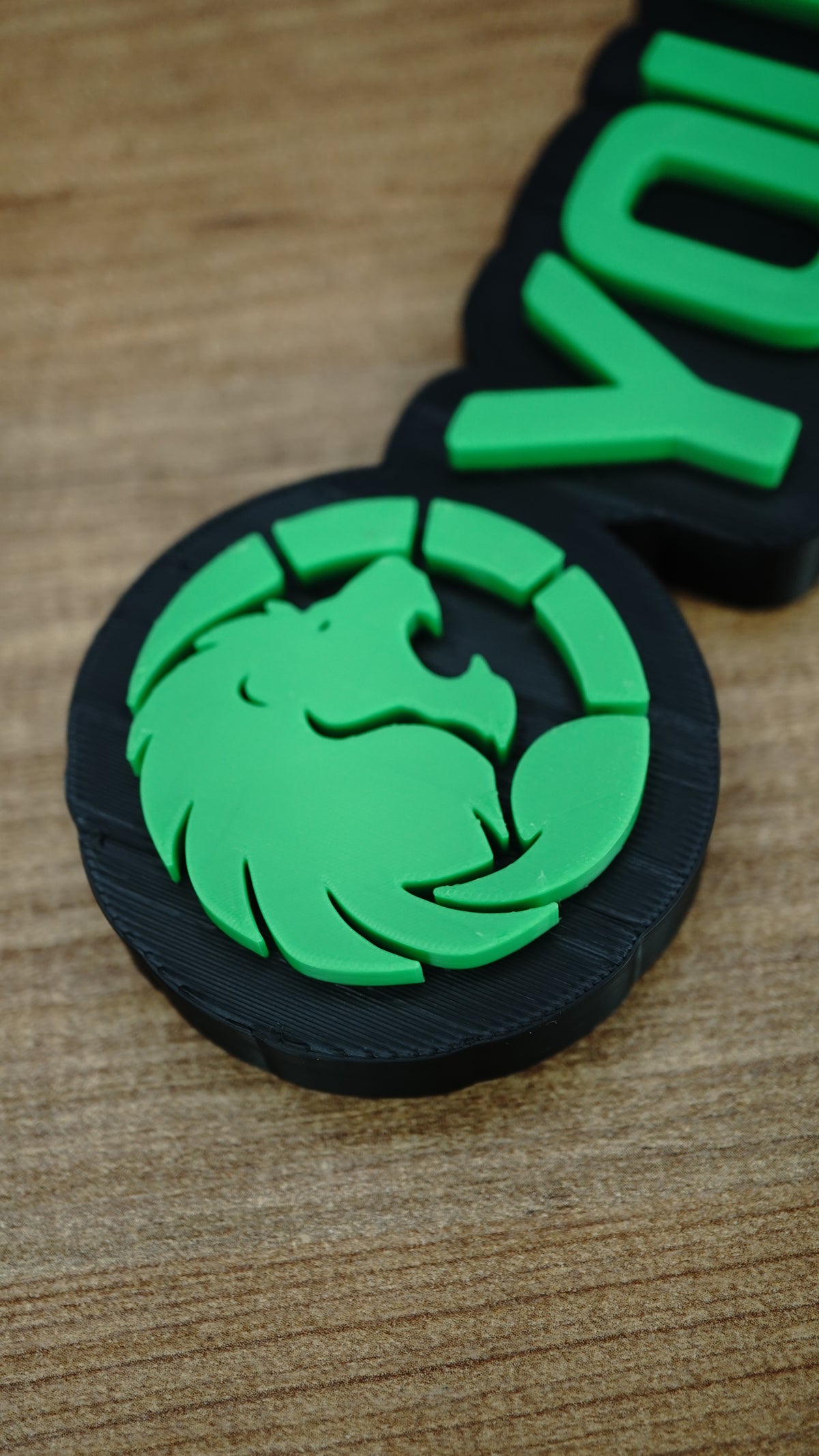 Close-up of the Manticore Green lion faction emblem with bright green raised detailing, a circular design and contrasting black nameplate backing.