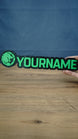 Manticore Green 25cm gaming nameplate held in one hand, showing the green lion emblem, YOURNAME lettering and full black outlined design against a blue background.