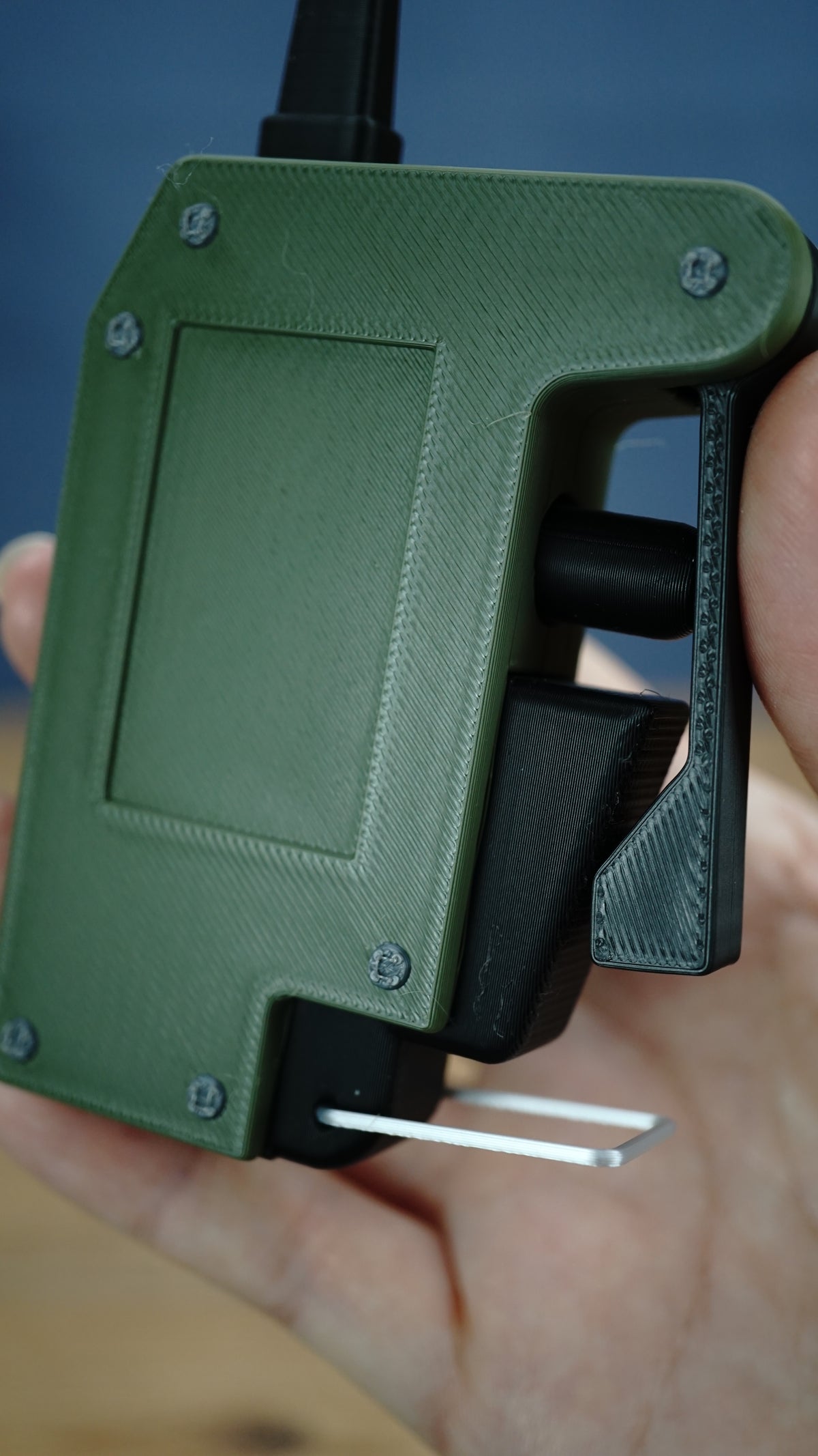 Close-up of the WARDOGS remote detonator fidget toy with textured olive green body, black trigger lever and movable side controls.