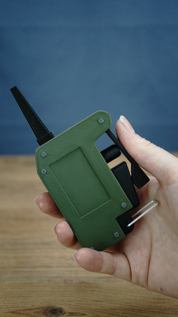 Handheld WARDOGS remote detonator replica in olive green and black, showing its side lever, clicker controls and compact gaming fidget design.