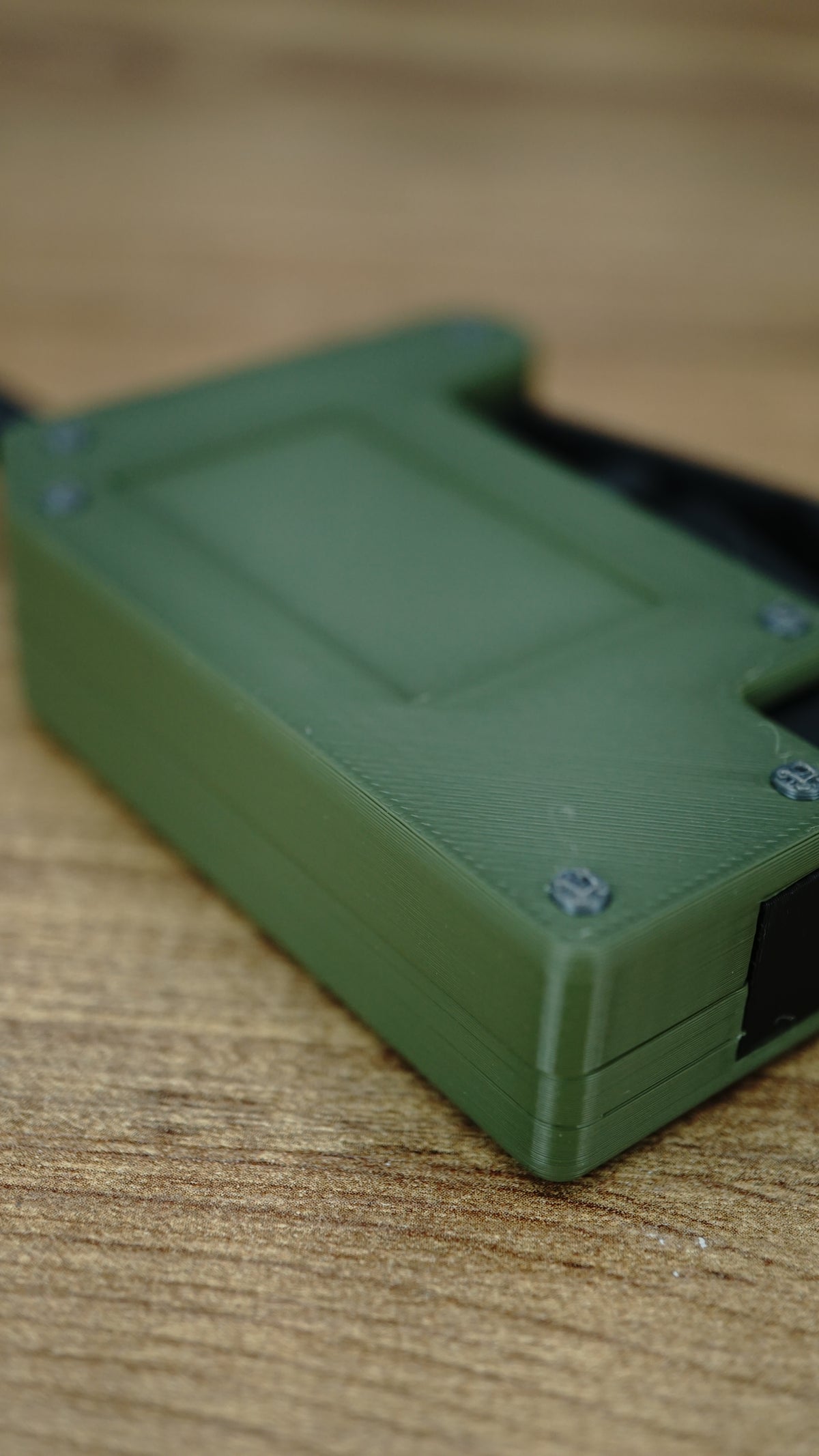 Angled macro view of the olive green WARDOGS remote detonator fidget toy, highlighting the casing edges and textured surface.