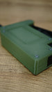 Angled macro view of the olive green WARDOGS remote detonator fidget toy, highlighting the casing edges and textured surface.