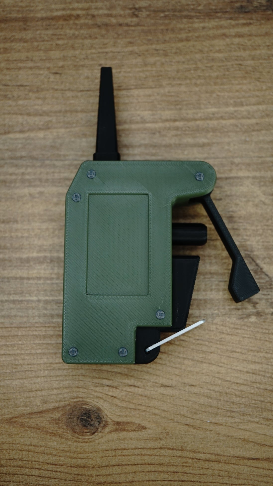 WARDOGS remote detonator gaming prop replica laid flat on a wooden table, showing the green casing, black lever and silver loop.
