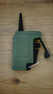 WARDOGS remote detonator gaming prop replica laid flat on a wooden table, showing the green casing, black lever and silver loop.
