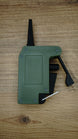 WARDOGS remote detonator gaming prop replica laid flat on a wooden table, showing the green casing, black lever and silver loop.