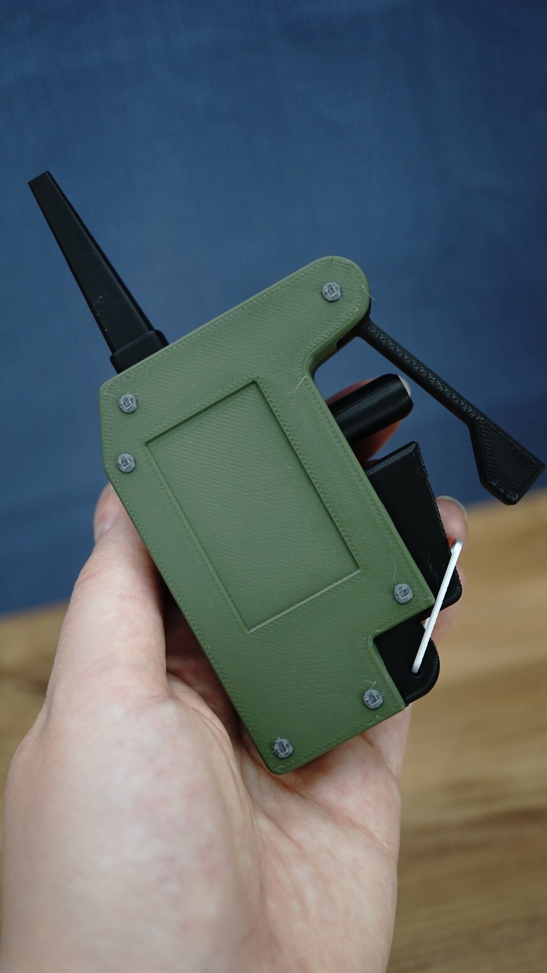 Handheld WARDOGS remote detonator fidget replica at an angle, showing its green panel, black clicker features and silver loop.