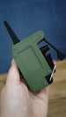 Handheld WARDOGS remote detonator fidget replica at an angle, showing its green panel, black clicker features and silver loop.