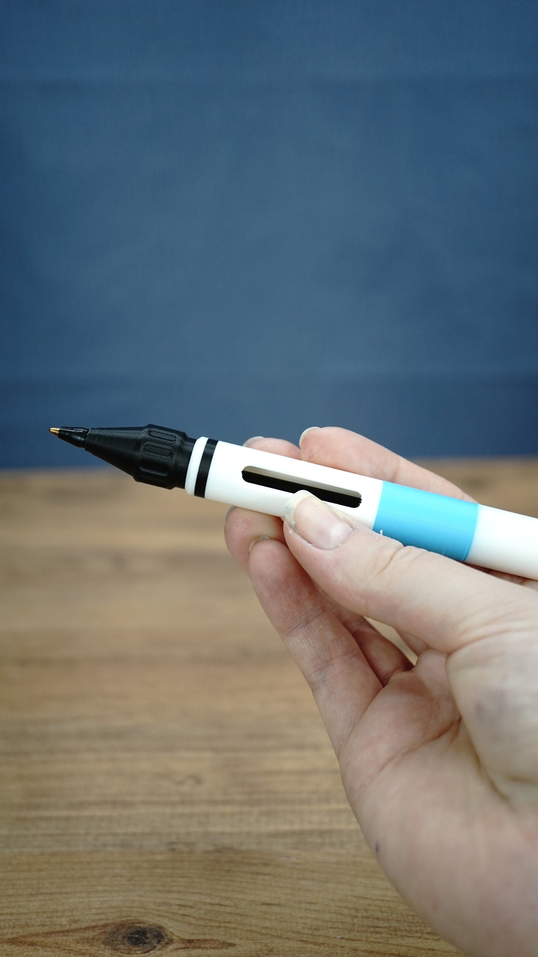 Hand holding the white and blue WARDOGS Adrenaline Stim Pen replica horizontally, showing the black writing tip and side opening of the casing.