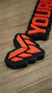Close-up angled photograph of the Valkyra Red faction emblem, showing raised red-orange geometric shapes on the black gaming nameplate base.