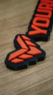 Close-up angled photograph of the Valkyra Red faction emblem, showing raised red-orange geometric shapes on the black gaming nameplate base.