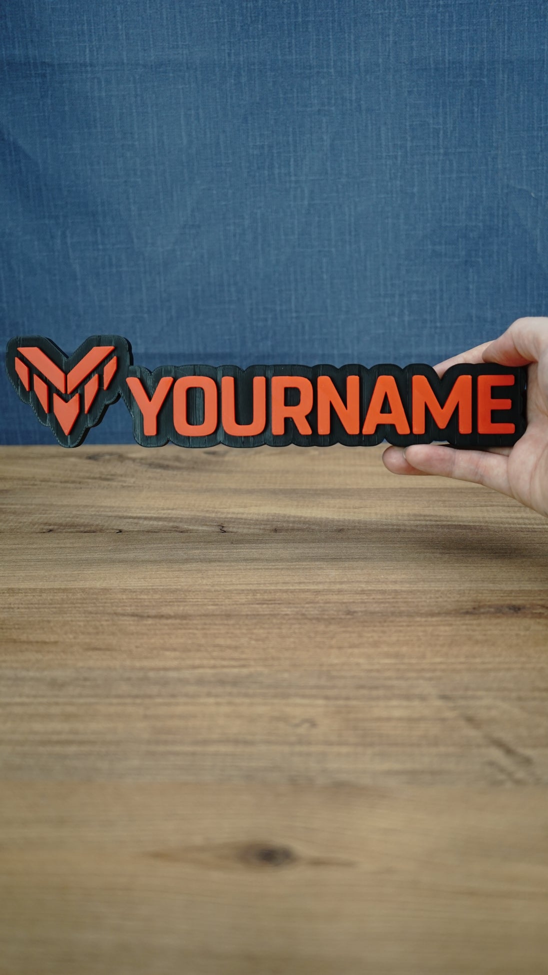 Valkyra Red 25cm gaming nameplate held in one hand, featuring raised red-orange YOURNAME lettering and an angular emblem on a black base.