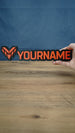 Valkyra Red 25cm gaming nameplate held in one hand, featuring raised red-orange YOURNAME lettering and an angular emblem on a black base.