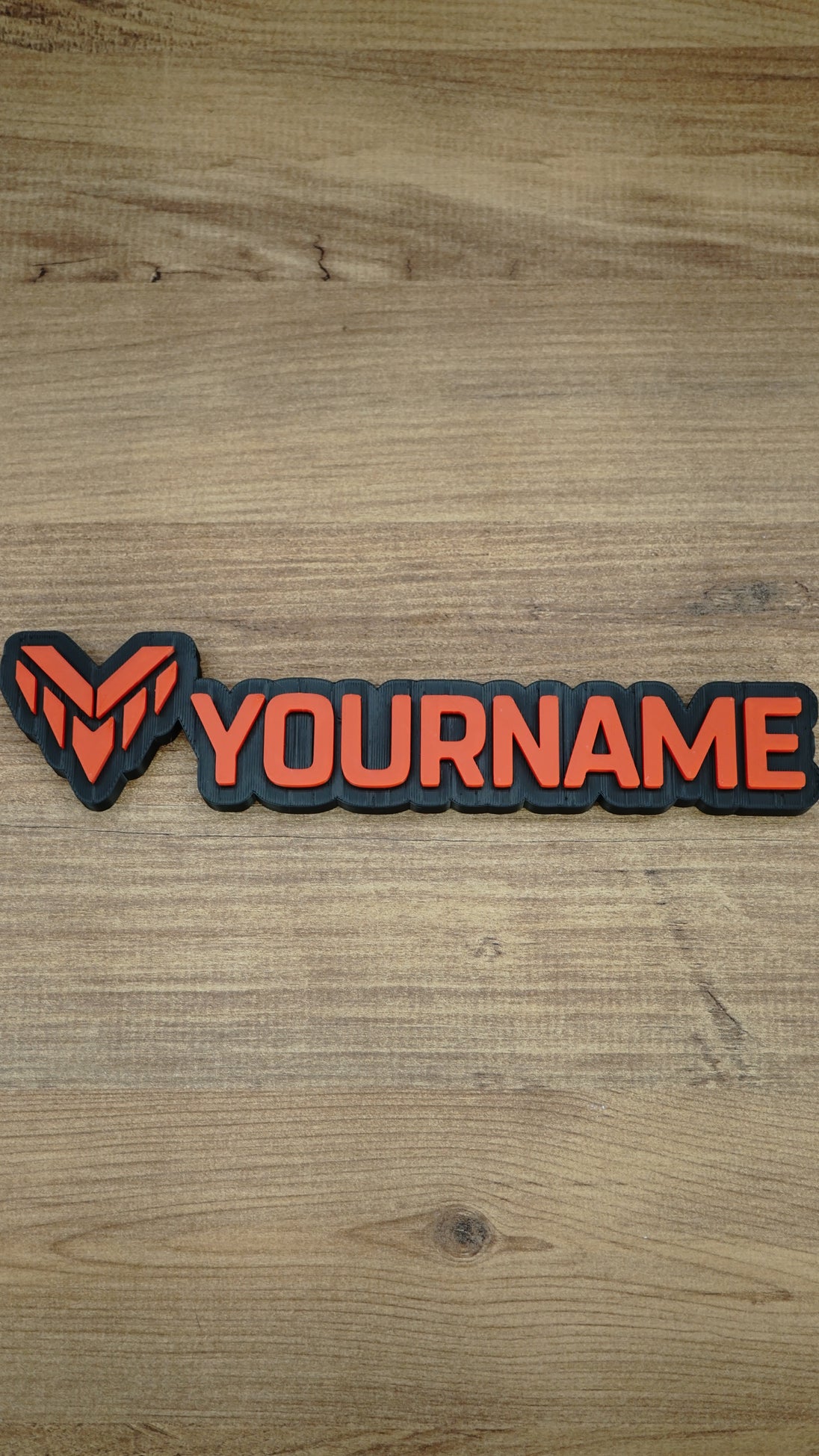 Overhead photograph of a Valkyra Red gaming nameplate featuring an angular red-orange faction emblem and YOURNAME lettering on a black backing.